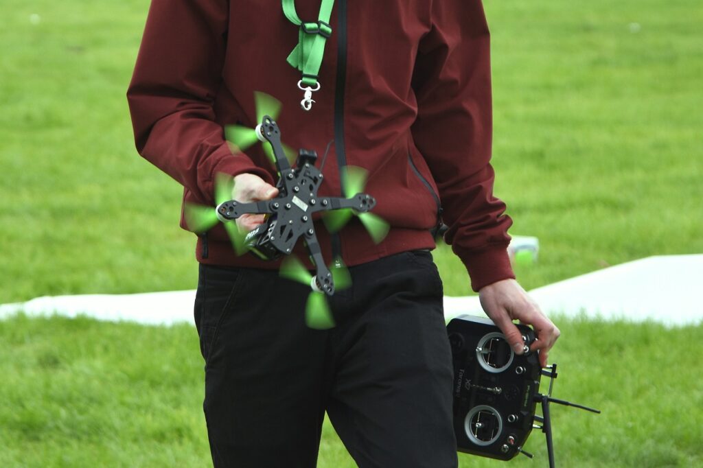 Pilot holding a drone and the remote on a green field.